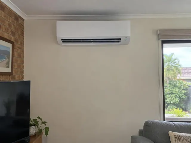 Wall-mounted split system running in a living room with brick feature wall and window in Elanora