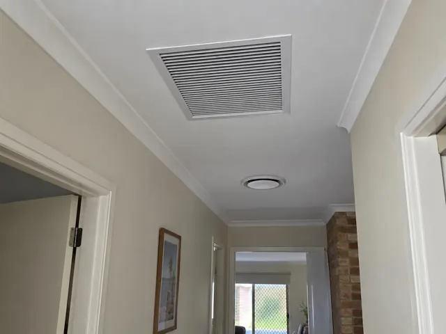 Ceiling return-air grille in a beige hallway with white trim and brick feature wall in Currumbin Waters