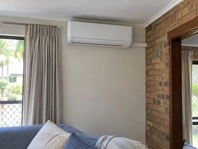 Wall-mounted split system above curtains in a brick-and-plaster living room in Palm Beach